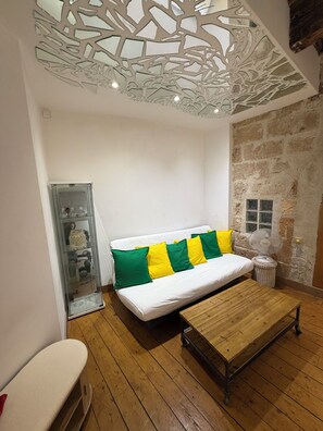 Une pièce avec un canapé blanc, des coussins verts et jaunes, une table basse en bois et une vitrine contenant des objets décoratifs.