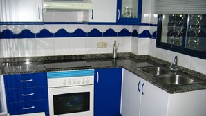 A kitchen with blue and white tiles, a stove, a sink, and a window with a view of the outside. - Canal Salinas, Bajo solo Familias (Xeraco Playa)