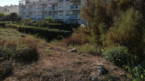 A multi-story residential building with balconies, surrounded by dense vegetation and a dry, grassy area. - Canal Salinas, Bajo solo Familias (Xeraco Playa)
