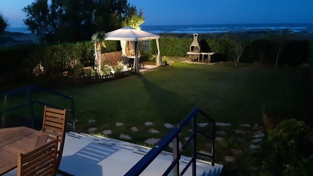 A patio with a table and chairs, a gazebo, and a grill area overlooking a grassy yard and ocean view. - Canal Salinas, Bajo solo Familias (Xeraco Playa)