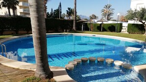 A swimming pool with a 'SPARKLING' tile pattern, surrounded by palm trees and a clear sky. - Canal Salinas, Bajo solo Familias (Xeraco Playa)