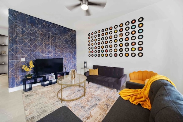 Un salon avec un téléviseur, un mur recouvert de disques vinyles, un canapé et une table basse.