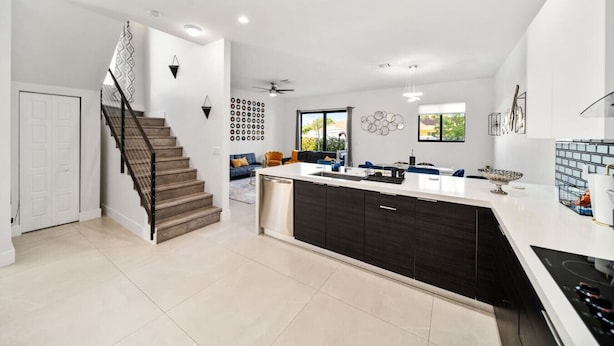 A modern kitchen with a central island, dark cabinetry, and a built-in dishwasher.