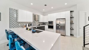 A modern kitchen with white cabinetry, a large island, blue bar stools, and stainless steel appliances.