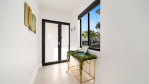 A hallway with a sliding glass door, a small table with a laptop, and a window with a view of palm trees.