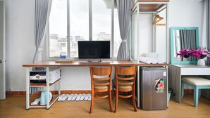 A compact hotel room with a wooden desk, two chairs, a small refrigerator, a TV, a mirror, and a window with curtains. - Huyen Home (Ho Chi Minh City)
