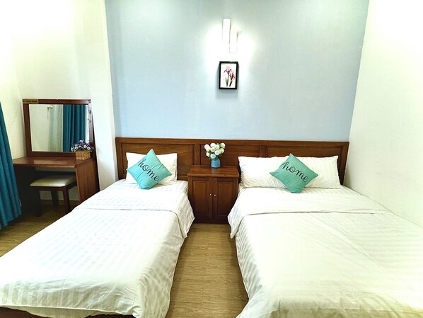 A hotel room with two beds, a wooden desk, a mirror, and a wall-mounted light fixture. - Huyen Home (Ho Chi Minh City)