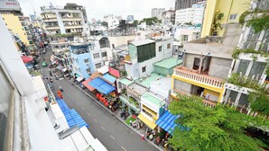 A bustling urban street with multi-story buildings, shops, and a variety of vehicles. - Huyen Home (Ho Chi Minh City)