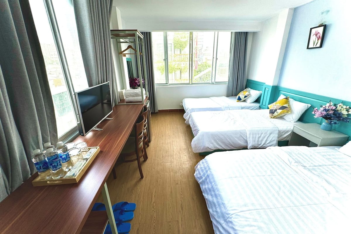 Een hotelkamer met twee bedden, een houten bureau met een dienblad waterflesjes, een televisie en een raam met gordijnen.