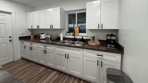 Cocina moderna con armarios blancos, encimera de granito, horno integrado y ventana sobre el fregadero.