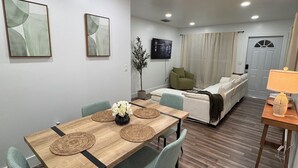 Una sala de estar moderna con comedor, un sofá y un televisor montado en la pared.