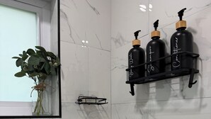 Un baño con baldosas de mármol, una planta en maceta y un estante con tres botellas negras.