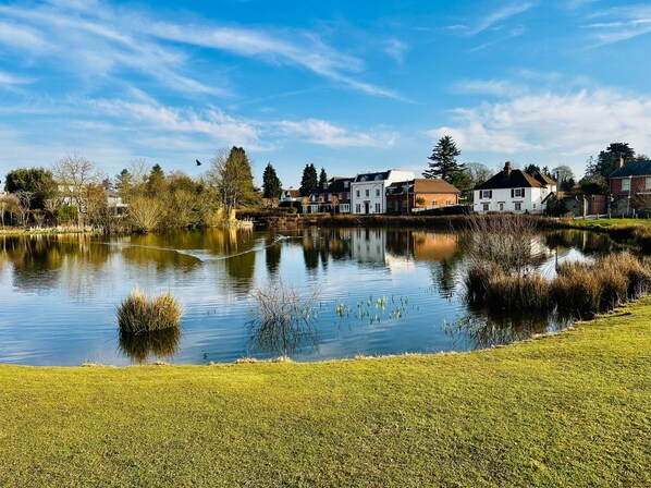 A calm lake with houses along the shore, clear skies, and a grassy foreground. - Gerrardscross - Stay4 - Parking - Petsok - Wembley (Gerrards Cross)