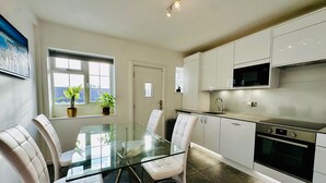 Una cocina moderna con armarios blancos, una mesa de comedor de vidrio y dos sillas.