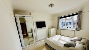 Un dormitorio con cama, mesita de noche, televisor, armario y ventana con cortinas.