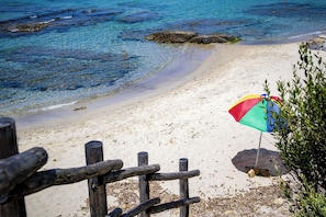 A beach with clear water, a sandy shore, and a colorful umbrella.