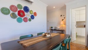 Un comedor con una mesa de madera, sillas color turquesa y una colección de platos de colores en la pared.