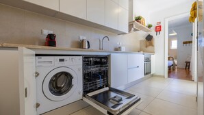 Una cocina moderna con lavadora integrada, cafetera y una planta colgante.