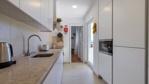 Una cocina moderna con armarios blancos, un hervidor de acero inoxidable, un tostador y un horno empotrado.