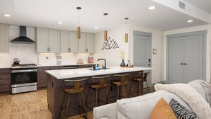 Una cocina moderna con una isla central, taburetes de bar, electrodomésticos de acero inoxidable e iluminación colgante.
