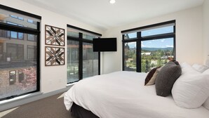 Un dormitorio moderno con una cama grande, dos ventanas, un televisor de pantalla plana y decoración en la pared.