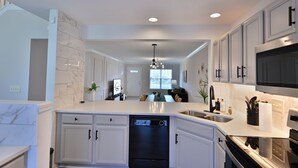 Una cocina moderna con armarios blancos, lavavajillas, microondas y un comedor con mesa y sillas.
