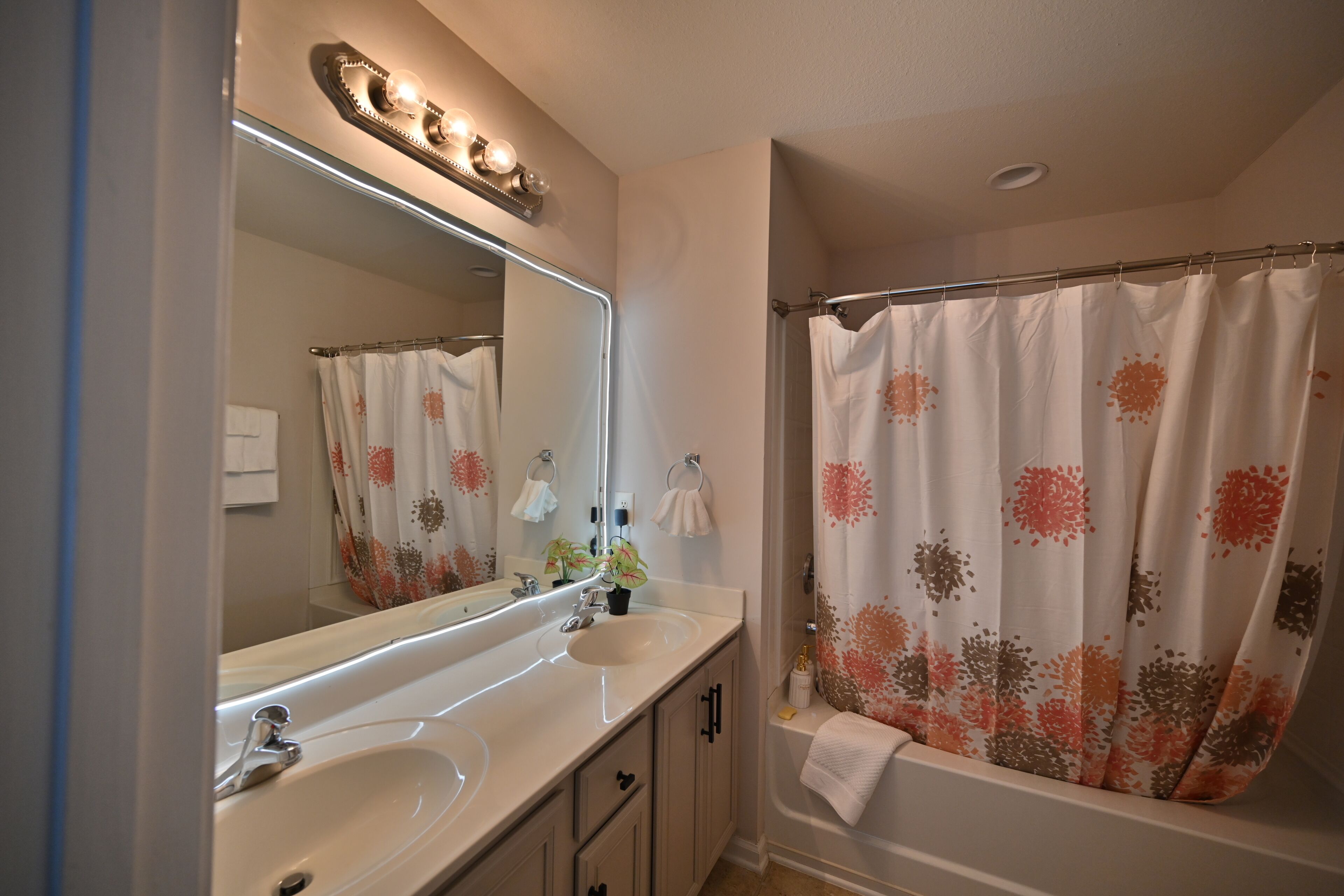 A bathroom with a double sink vanity, a large mirror, and a shower curtain with a floral pattern.