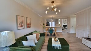 Una sala de estar moderna con un sof á verde, un reposapiés a juego, y un comedor con una mesa y sillas.
