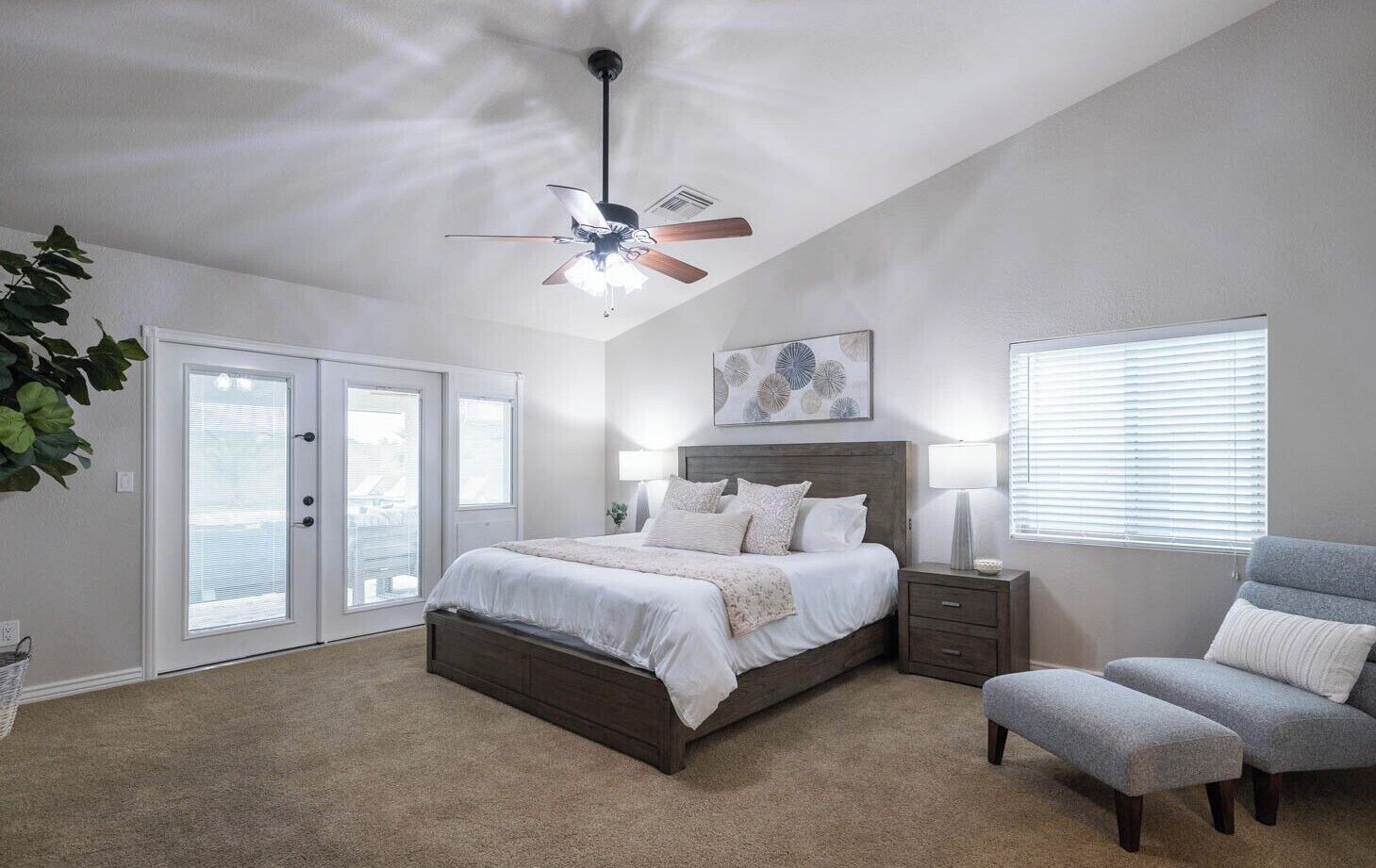 A bedroom with a bed, a ceiling fan, a nightstand, a chair, and a window with blinds.
