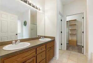Double sink vanity with a large mirror above, accompanied by a closet with open shelves.