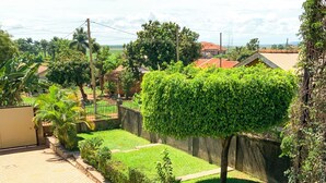 A well-maintained garden with a paved walkway, neatly trimmed hedges, and a variety of plants. - Hendo Hotel (Entebbe)
