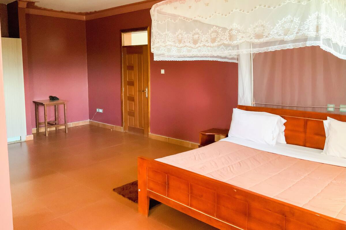 A bedroom with a wooden bed, a bedside table, a nightstand, a door, and a window with a white curtain.