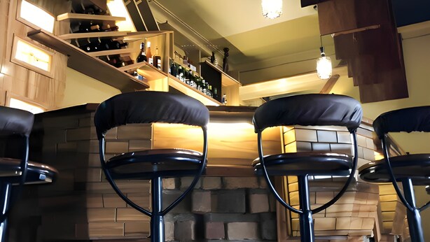 A bar area with a stone wall, wooden bar counter, and multiple stools. - Hendo Hotel (Entebbe)