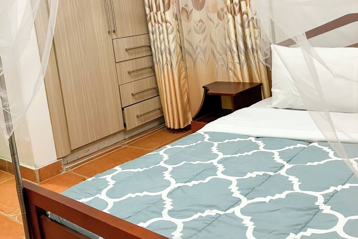 A bedroom with a bed, wooden headboard, a nightstand, a wardrobe, and a curtain with a floral pattern.