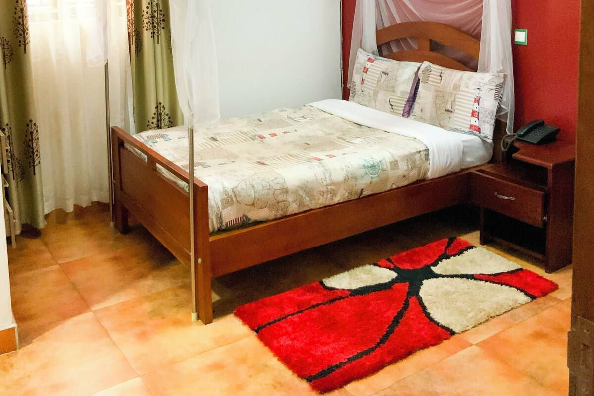 A single bed with a canopy, a bedside table with a phone, and a red and white patterned rug.