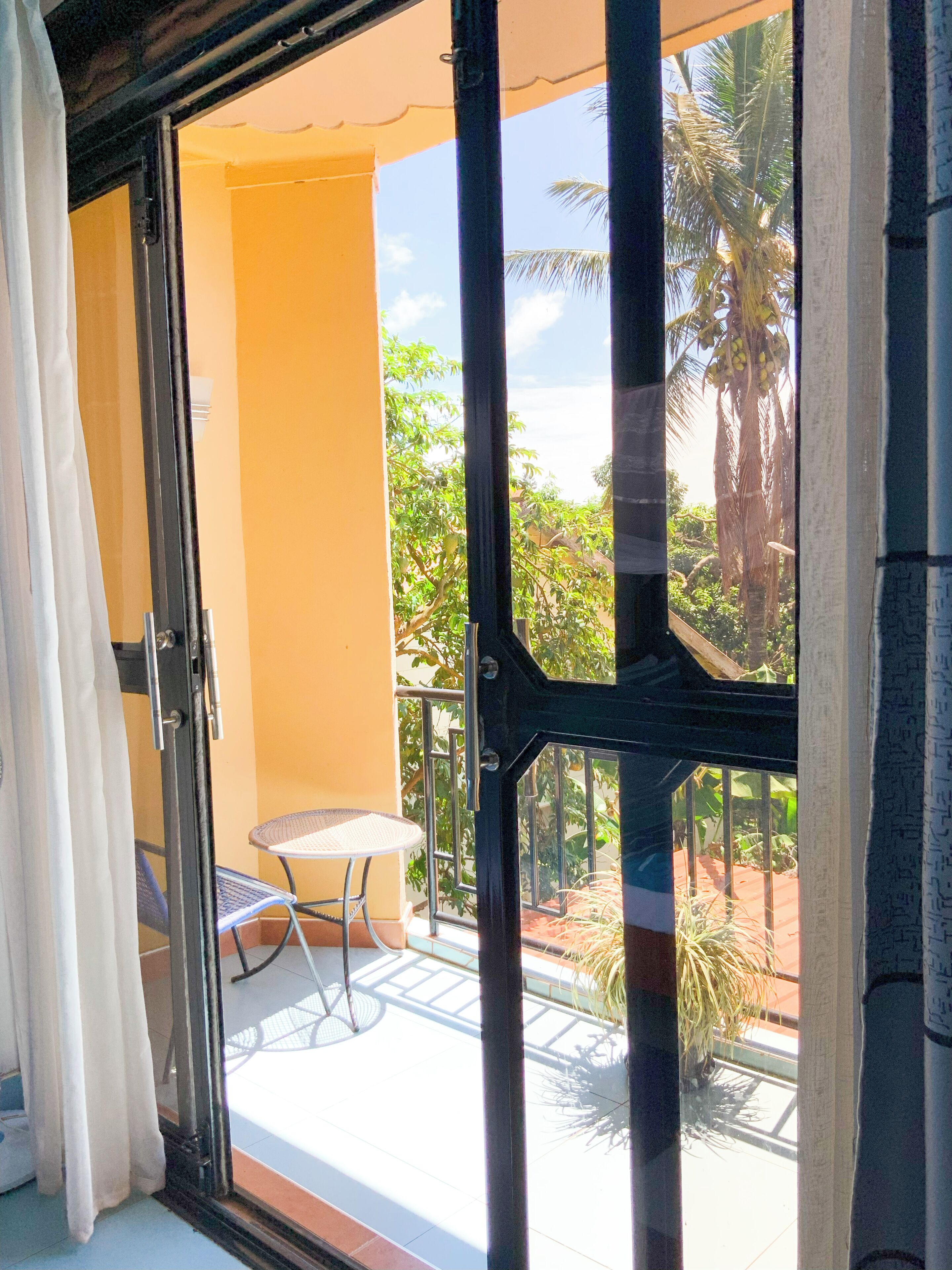 Un balcone con tavolo e sedie, vista su palme e un muro giallo.