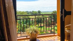 A balcony with a potted plant, a view of greenery, and a clear sky. - Hendo Hotel (Entebbe)