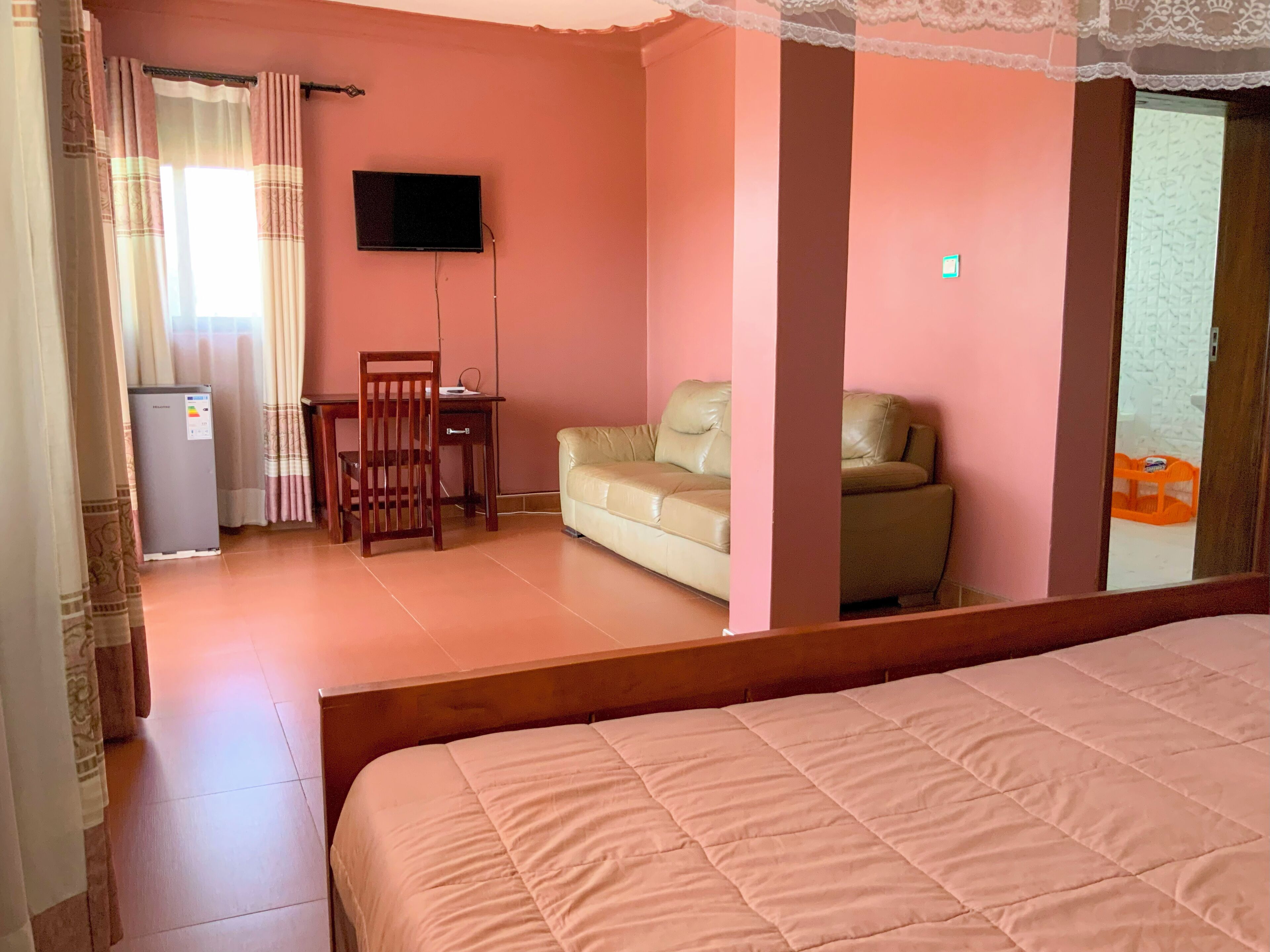 A hotel room with a bed, a sofa, a TV, a desk, and a refrigerator.