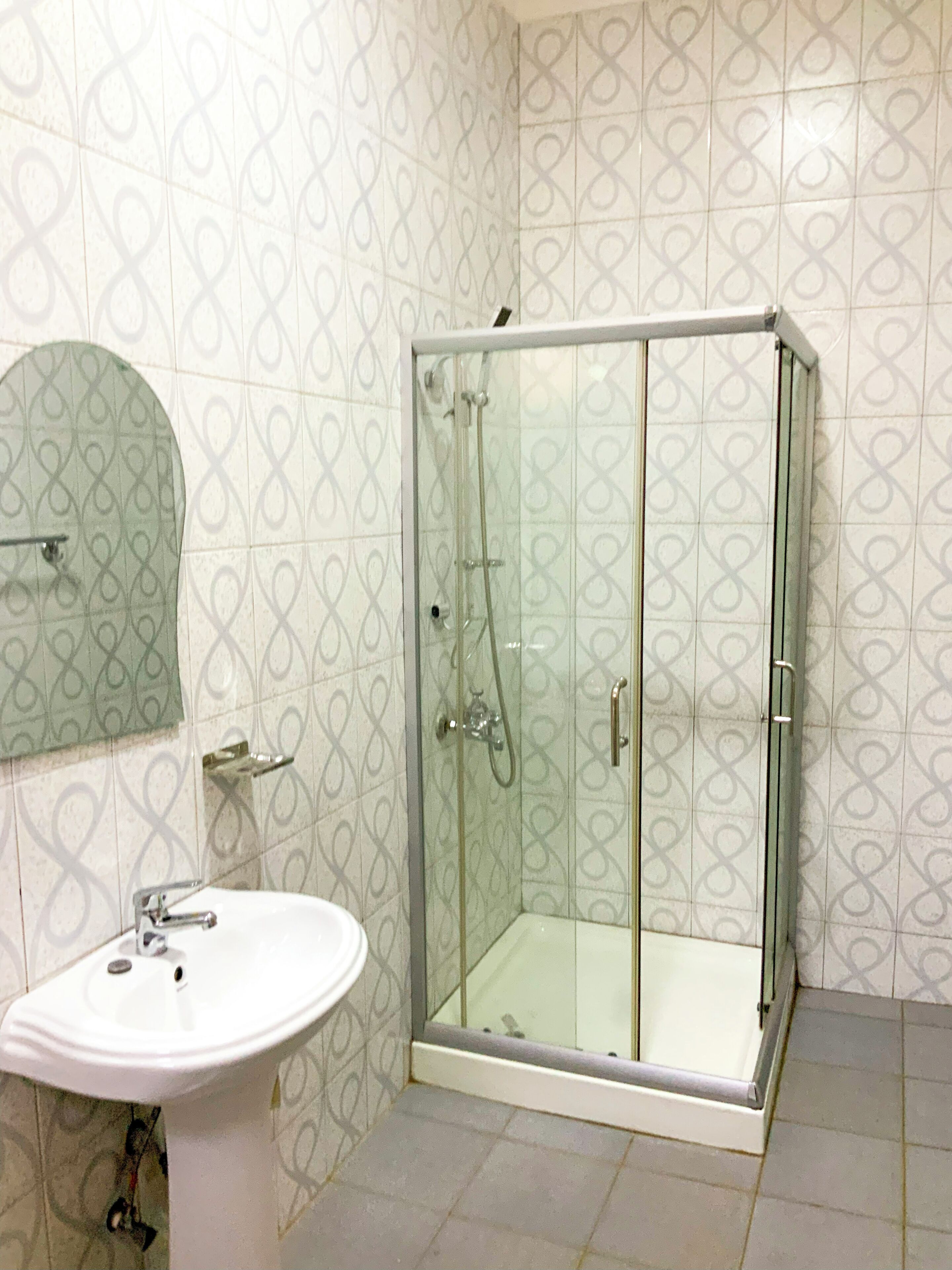 Een badkamer met een douche met glazen wand, een wastafel op een voetstuk en een spiegel met decoratieve lijst.