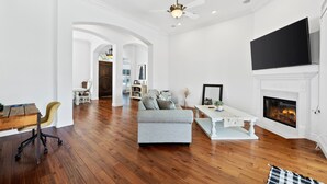 Ein geräumiges Wohnzimmer mit Holzboden, einem grauen Sofa, einem weißen Couchtisch und einem Kamin.