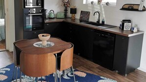 A modern kitchen with a central island, black cabinetry, and a dining area with a wooden table and chairs. - Gîte Du Vieux Chêne (Plaine)