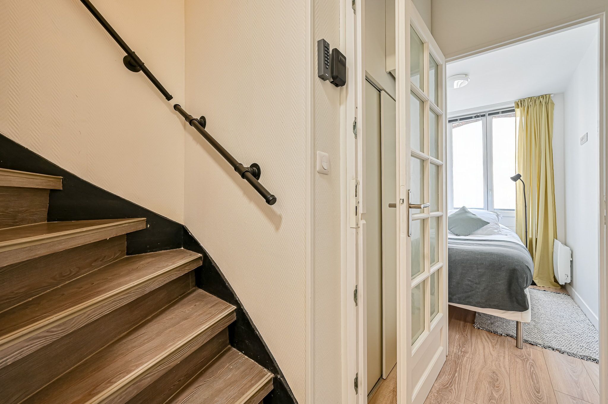 A staircase leading to a bedroom with a bed, a window with curtains, and a radiator.