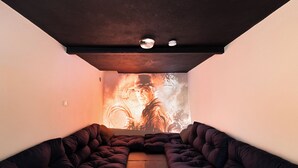 Une pièce moderne avec un canapé aux couleurs sombres, placé face à un grand écran diffusant une scène de film.