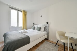 Une chambre à coucher moderne avec un lit, une table de chevet, une chaise et une fenêtre avec des rideaux.