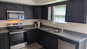 A modern kitchen with dark cabinetry, stainless steel appliances, and a window with blinds.