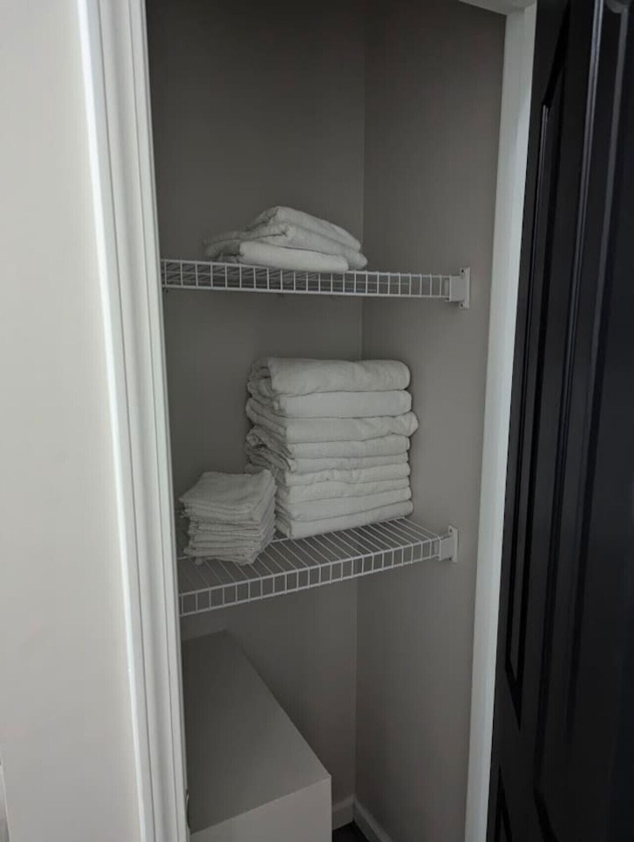 Un placard avec trois étagères blanches, chacune contenant des serviettes pliées.