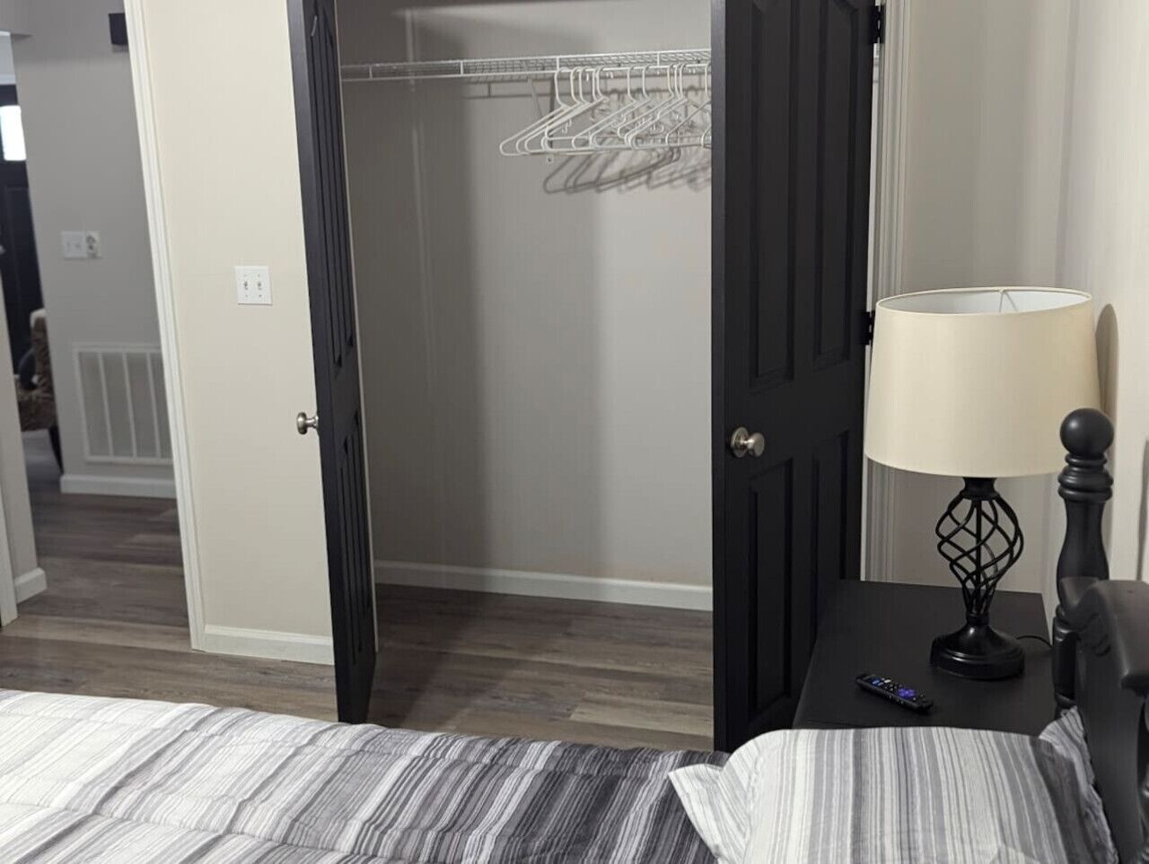 A bedroom with a bed, a nightstand with a lamp, and an open closet with hanging clothes.