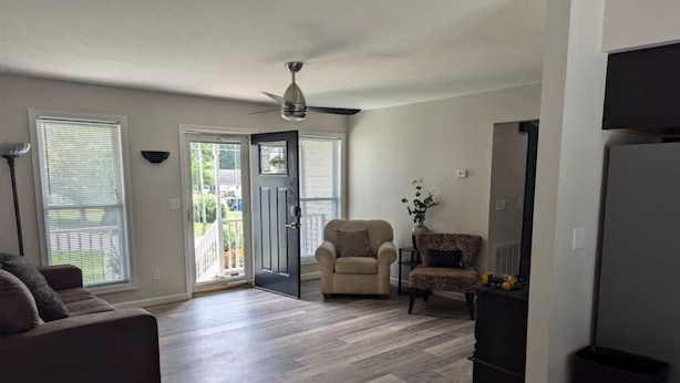An open-plan living area with a sofa, two armchairs, a ceiling fan, and a door leading to a balcony.