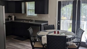 A modern kitchen with dark cabinetry, a dining table with chairs, and a view through a glass door.