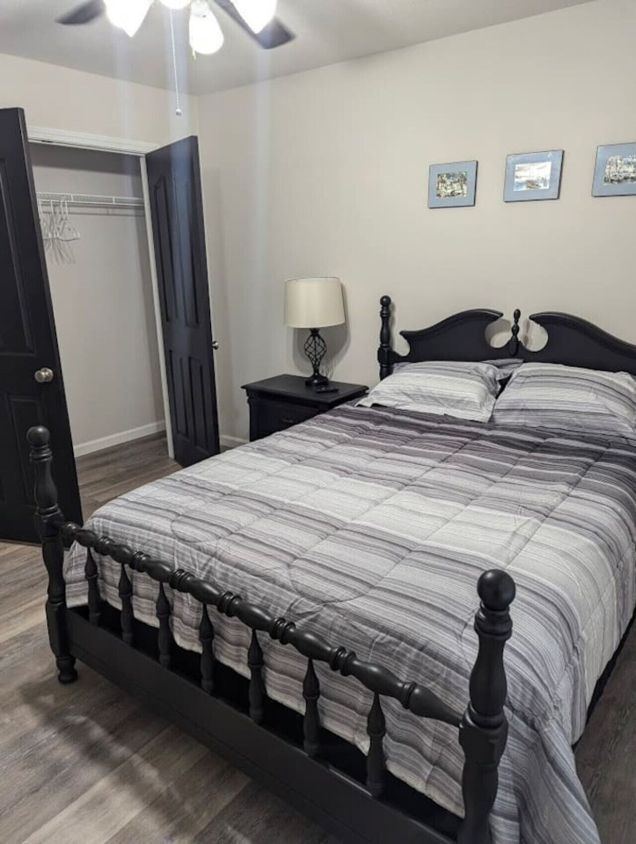 Um quarto com cama, mesa de cabeceira, abajur e quadros na parede.